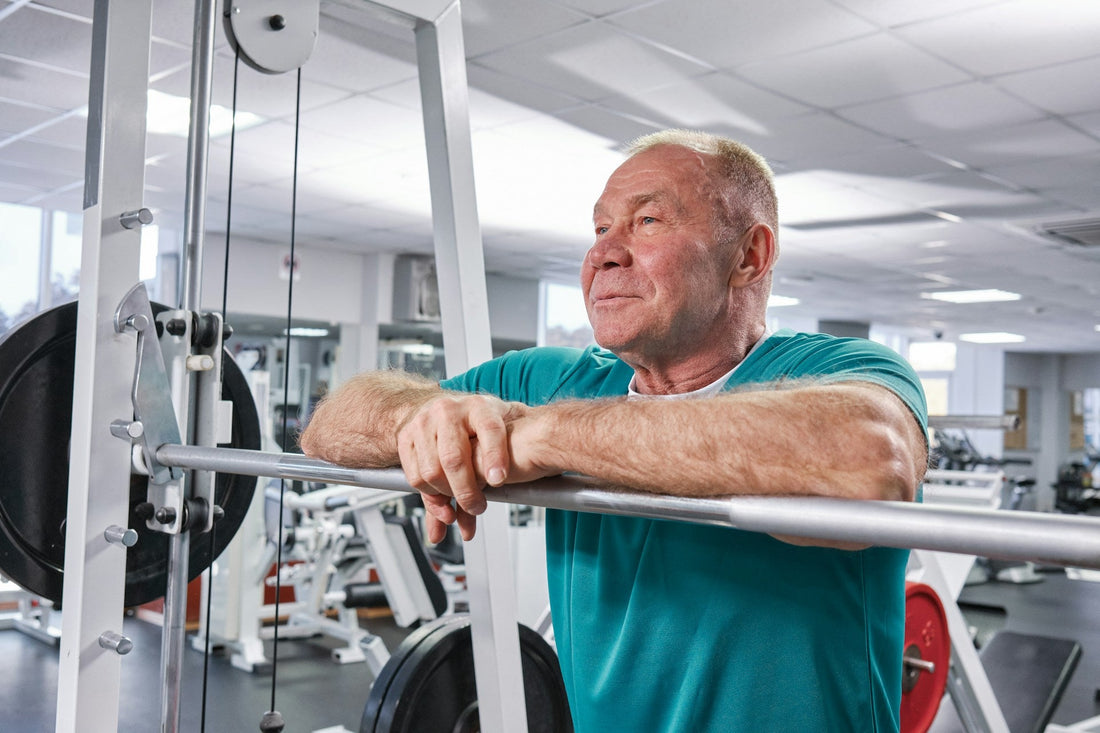 A senior man at the gym looking after himself, leaning on a weight’s bar