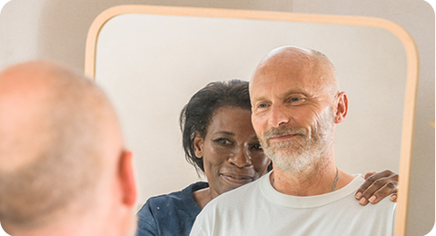 Man looking into a mirror with partner smiling behind him hold onto his shoulder